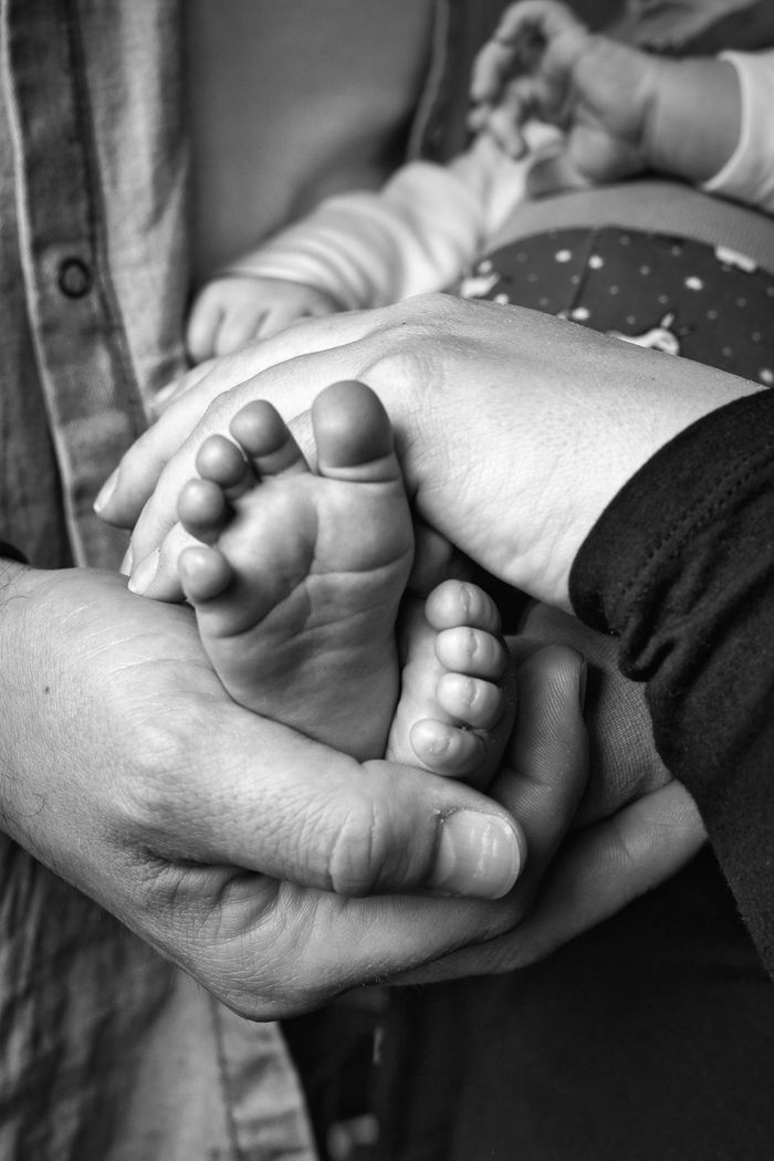 Black and white close-up of baby feet held in a parent's protective hands, conveying love and care.