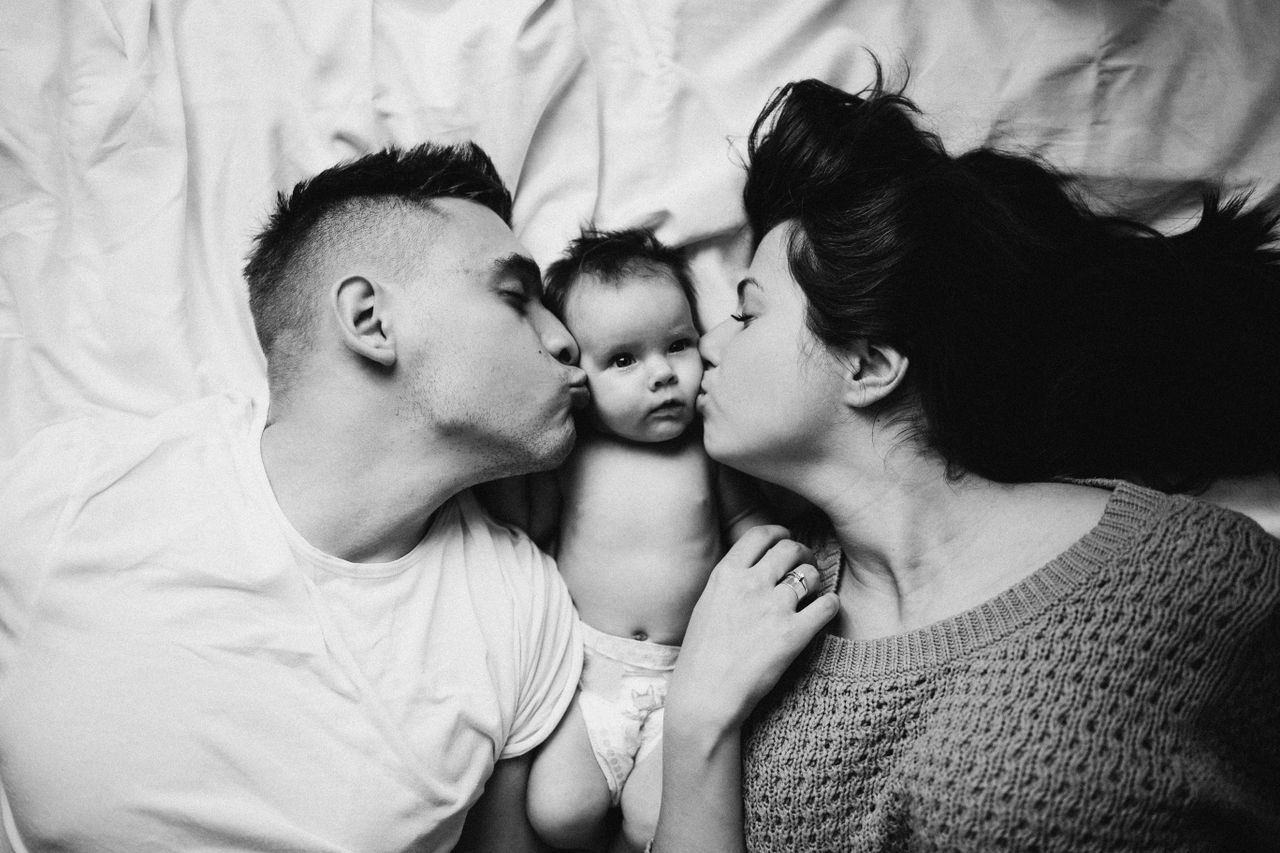 A tender black and white portrait of a couple kissing their baby, showcasing family love.