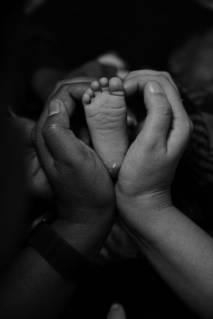 services-04 Black and white photo of a baby foot held by parents' hands symbolizing love and care.