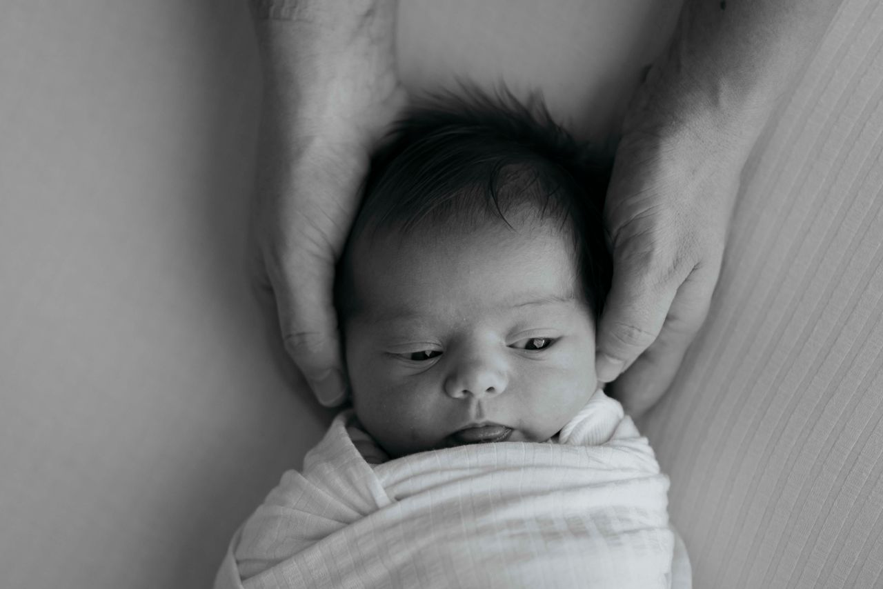 about-02 A peaceful newborn wrapped in white swaddle, cradled by comforting hands.