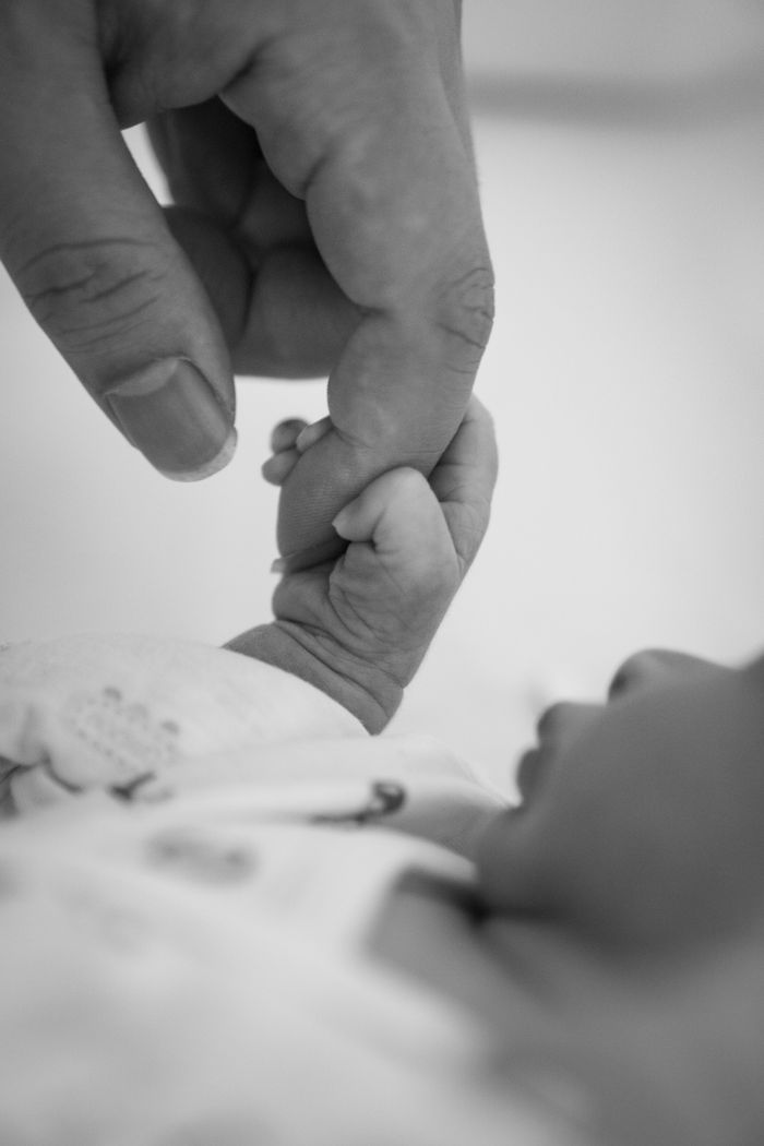 Black and white photo of a father and baby holding hands.